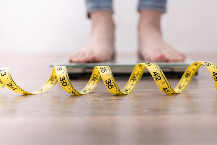 Close up of someone's feet standing on a sale with a tape measure in the foreground.