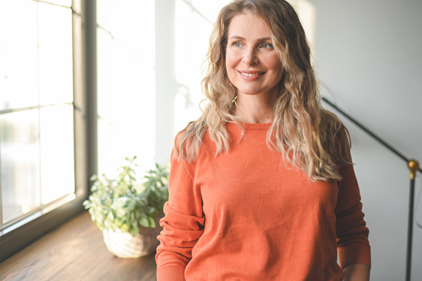 Woman standing at sunlit counter looking happy and contemplative. 