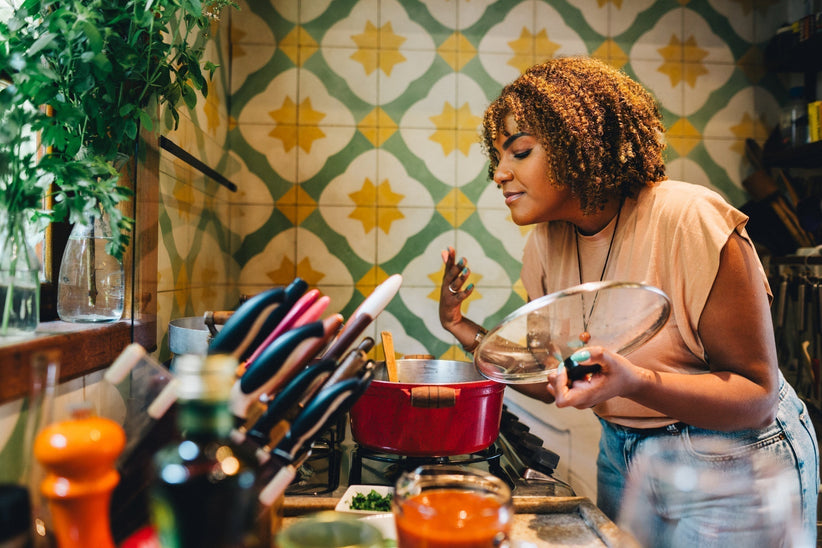 Woman smiling with her eyes closed while smelling food cooking in a pot on a stove in her kitchen at home