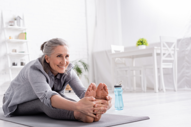 Woman stretching by grabbing her feet while sitting on a yoga mat.